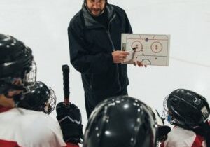 A women's ice hockey coach is writing up a play on a white board before the hockey game. The women look at him with purpose. Image taken in Utah, USA.
