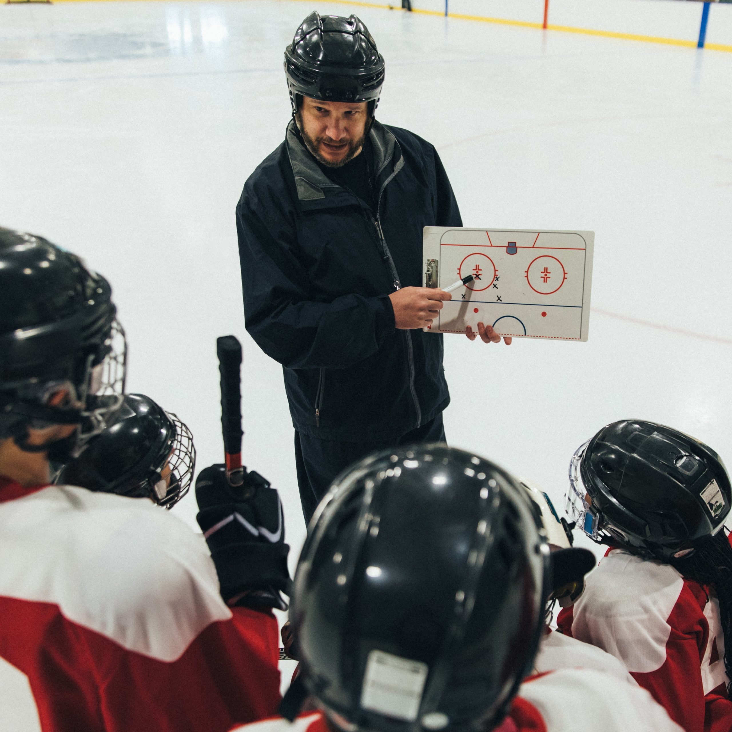 A women's ice hockey coach is writing up a play on a white board before the hockey game. The women look at him with purpose. Image taken in Utah, USA.
