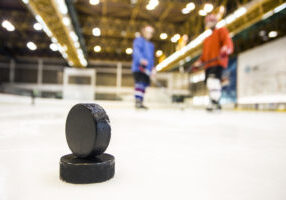 Ice hockey pucks at the ice rink, in front of unrecognizable ice hockey players.